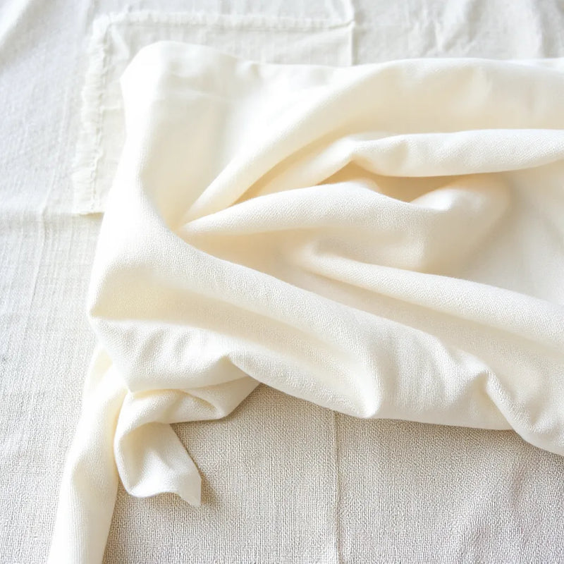Light beige cotton fabric with visible weave texture and soft folds in natural daylight