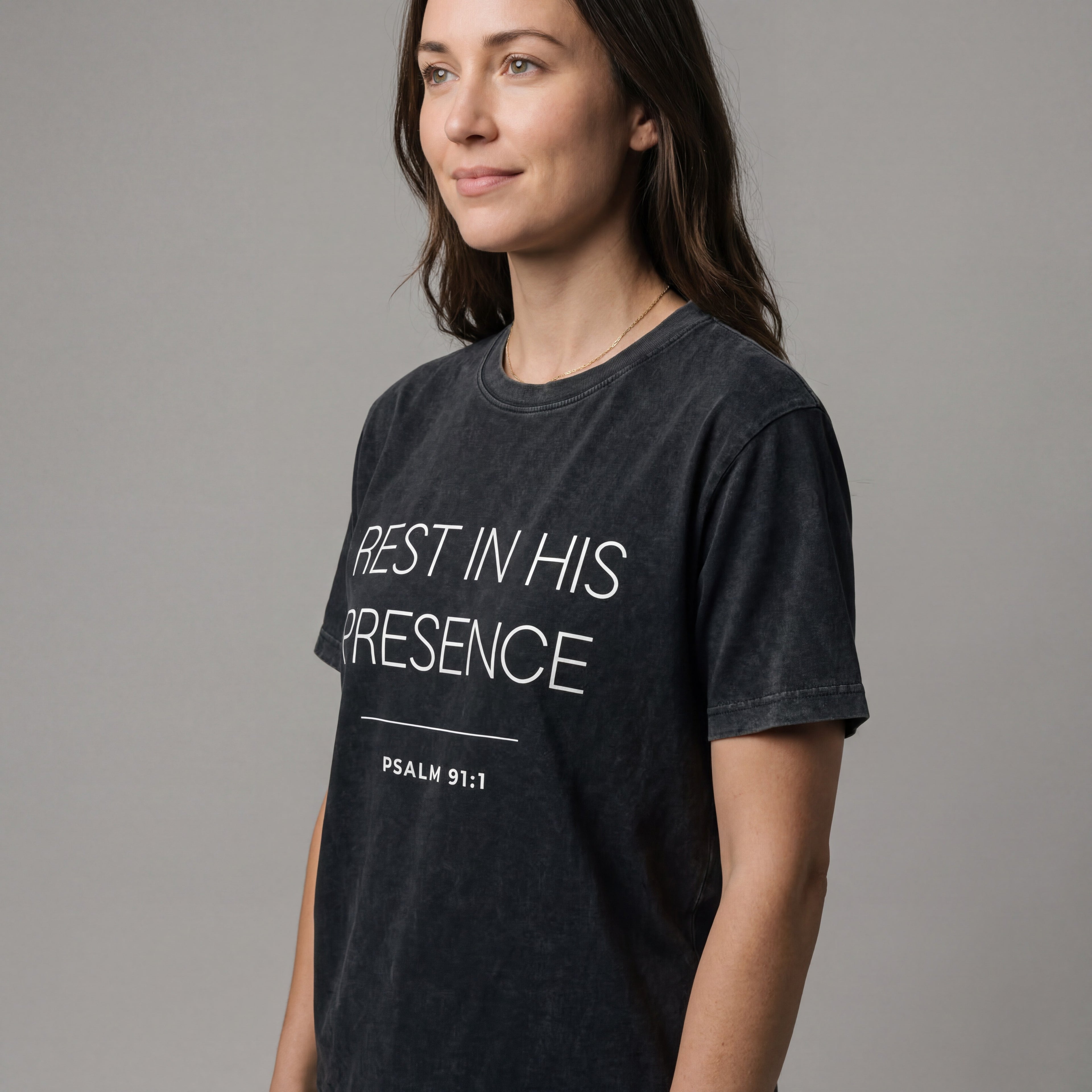 Side angle studio view of a woman wearing the "abide in his presence psalm 91:1" minimalist graphic tee with a calm, natural expression.