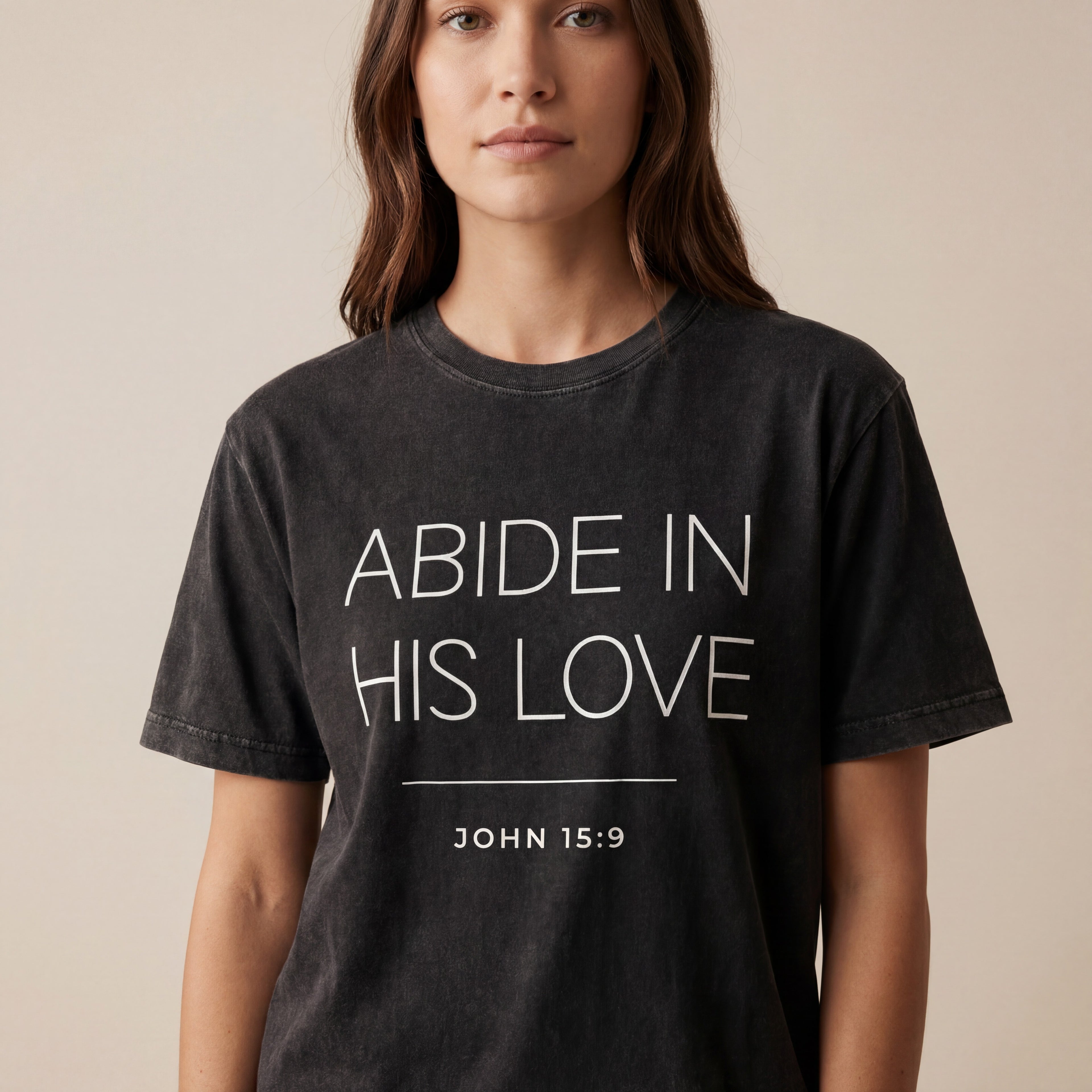 Woman wearing the "abide in his love john 15-9" minimalist graphic tee in a soft neutral studio setting, calm and welcoming.