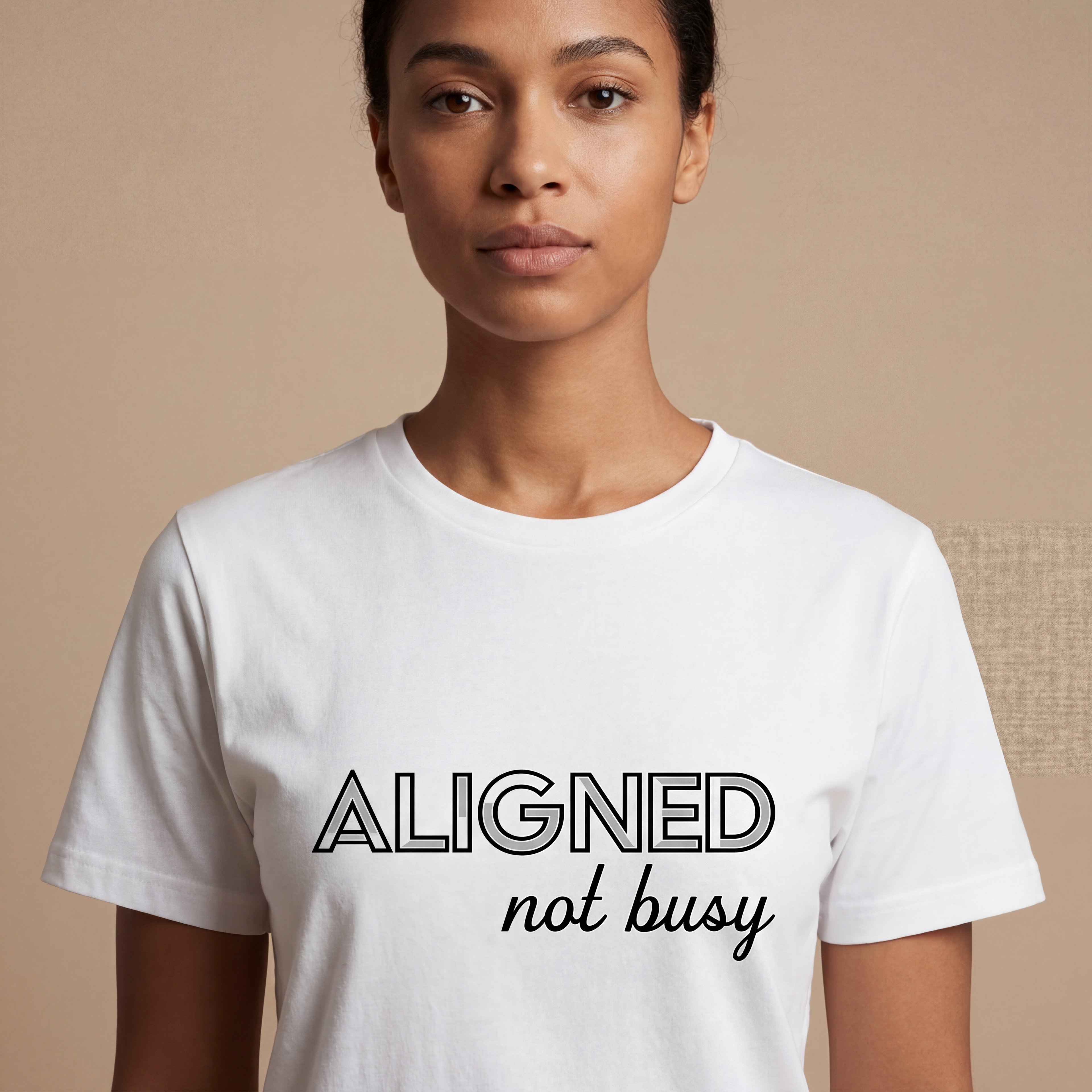 Woman wearing the "aligned not busy" minimalist graphic tee in a soft neutral studio setting, calm and welcoming.