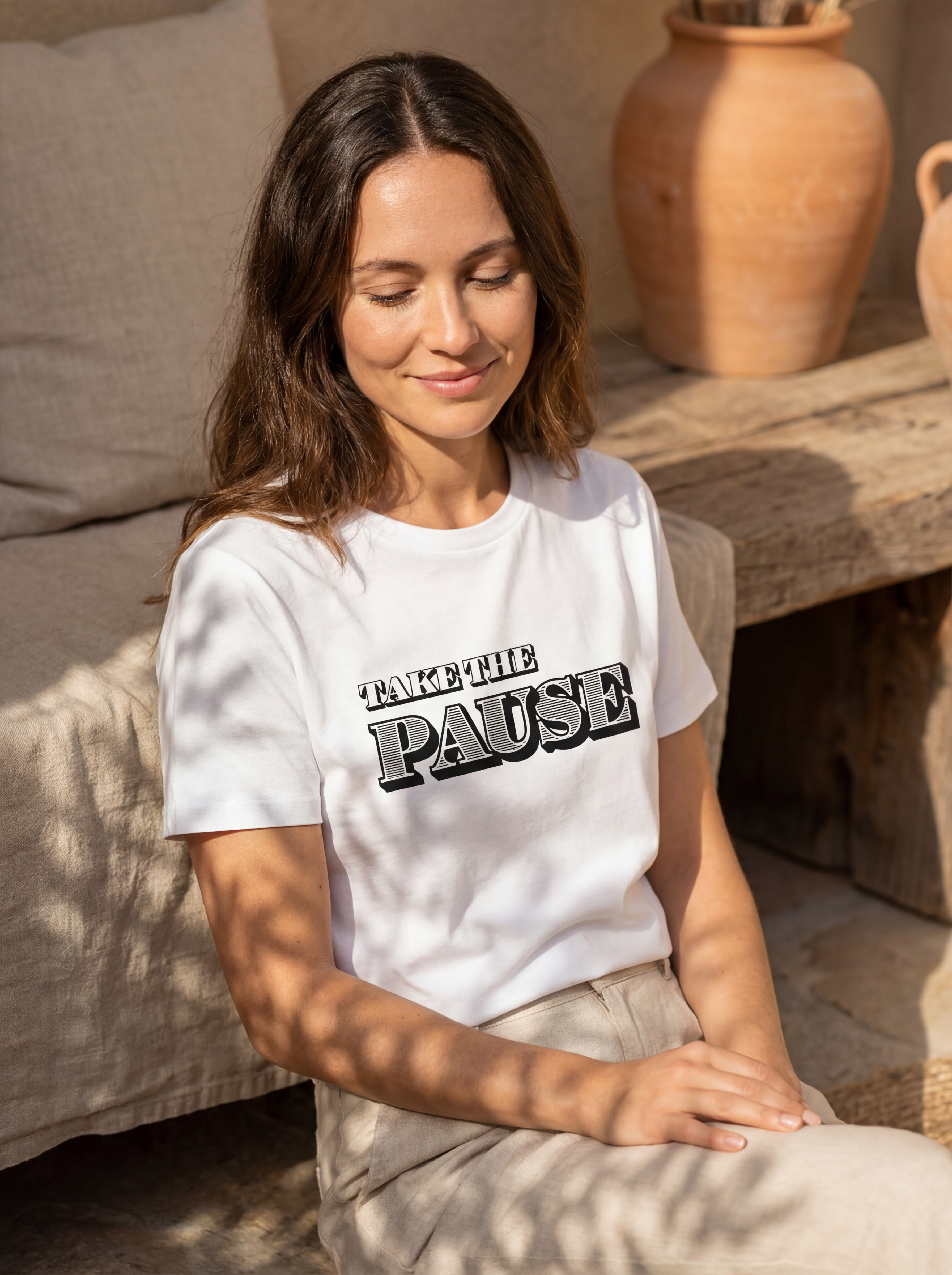 Woman wearing the Take the pause motivational t‑shirt in warm natural sunlight with a peaceful, reflective mood.